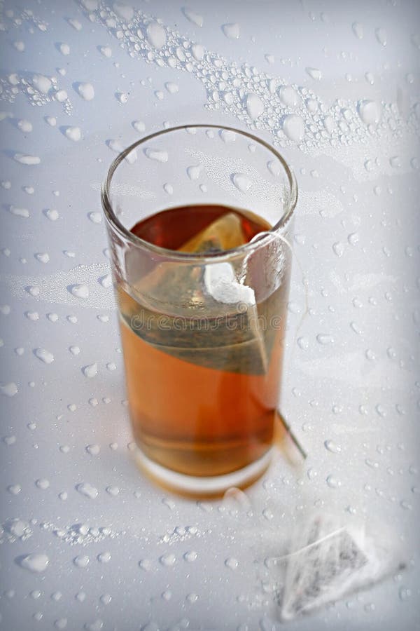 Black tea in a glass with piramid teabag on a side on water drops background. Black tea in a glass with piramid teabag on a side on water drops background