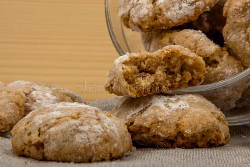 Transparent glass jar with Italian almond-flavored cookies amaretti dropped out on gray linen cloth on a wooden table, close up. Transparent glass jar with Italian almond-flavored cookies amaretti dropped out on gray linen cloth on a wooden table, close up