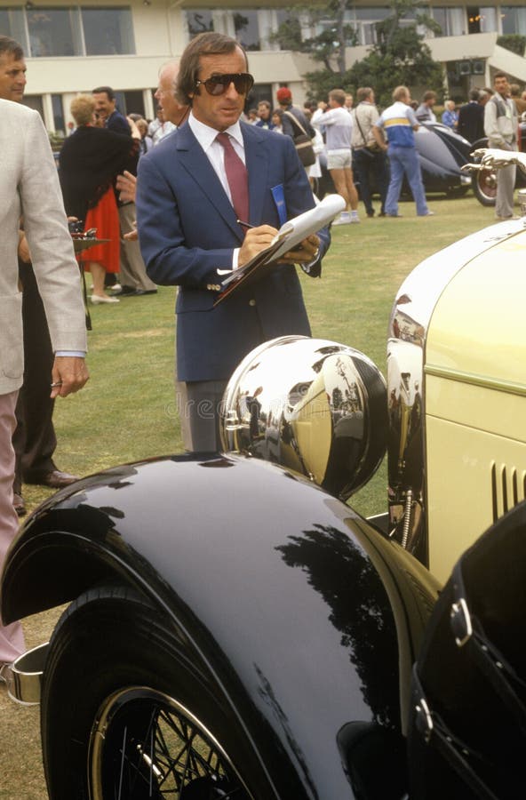 Szkocki samochodu wyścigowego kierowca Jackie Stewart egzamininuje rocznika Bugatti samochód w otoczak plaży, Kalifornia, ca 1985 zdjęcie royalty free Szkocki samochodu wyścigowego kierowca Jackie Stewart egzamininuje rocznika Bugatti samochód w otoczak plaży, Kalifornia, ca 1985 zdjęcie royalty free