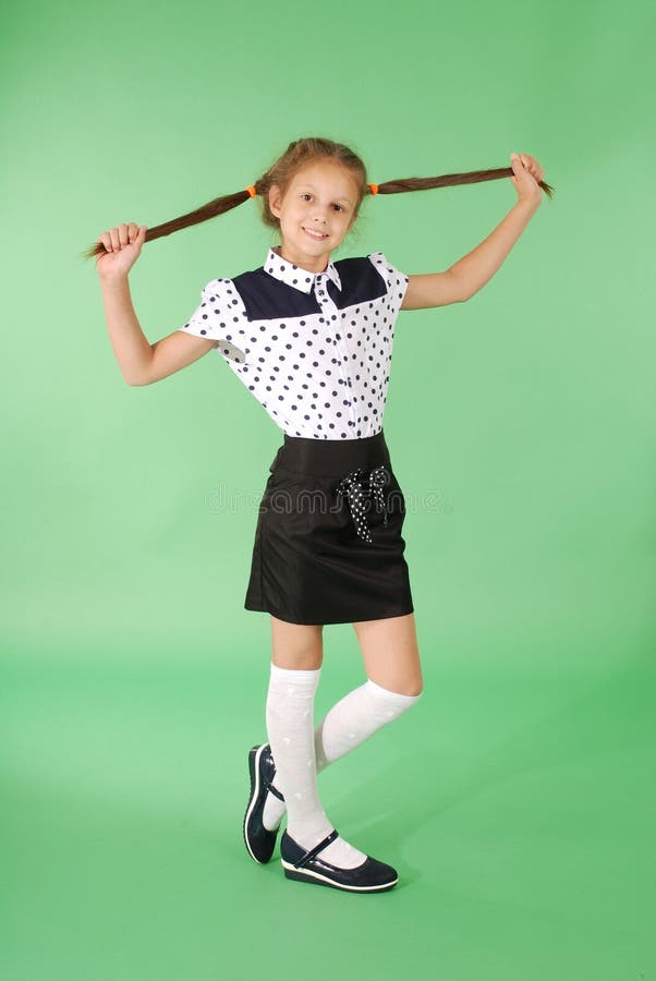 School girl plays with plaited hair. Lovely girl hold plait of hair in hands and look in the camera on green. School girl plays with plaited hair. Lovely girl hold plait of hair in hands and look in the camera on green