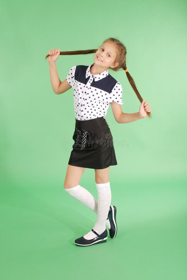 School girl plays with plaited hair. Lovely girl hold plait of hair in hands and look in the camera on green. School girl plays with plaited hair. Lovely girl hold plait of hair in hands and look in the camera on green