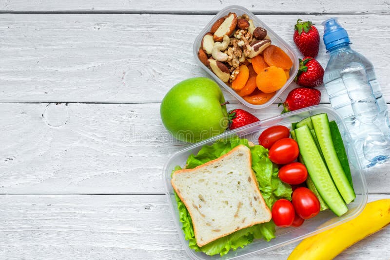 School lunch boxes with sandwich and fresh vegetables, bottle of water, nuts and fruits on white wooden background. healthy eating concept. top view with copy space. School lunch boxes with sandwich and fresh vegetables, bottle of water, nuts and fruits on white wooden background. healthy eating concept. top view with copy space