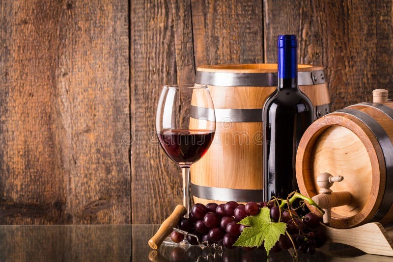 Glass of red wine with dark bottle barrel grapes and wooden background. Glass of red wine with dark bottle barrel grapes and wooden background