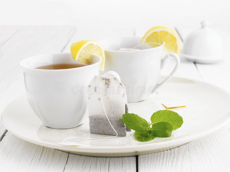 Two cups of green tea with teabag lemon and mint. Isolated on white background. Shallow focus, focus on teabag. Two cups of green tea with teabag lemon and mint. Isolated on white background. Shallow focus, focus on teabag.