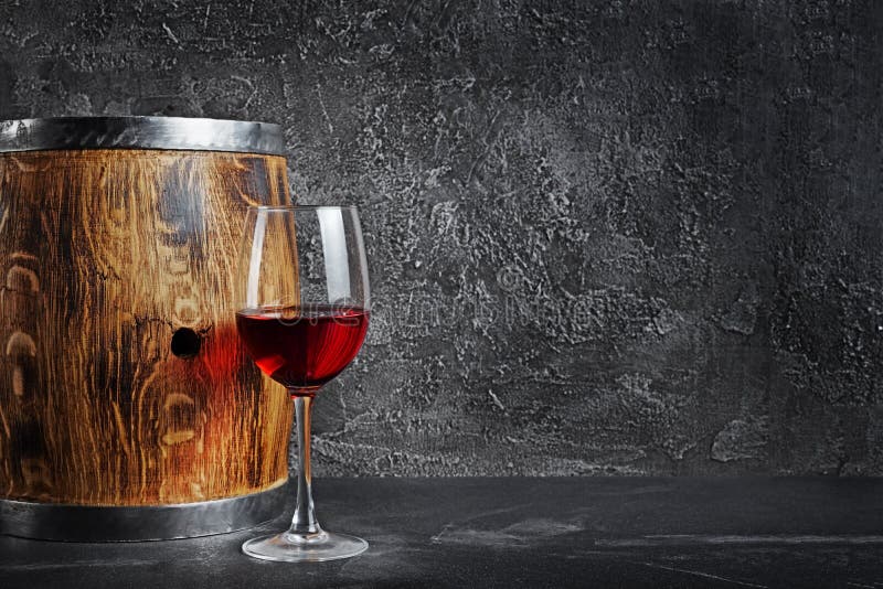 Glass with red wine for tasting and wooden barrel in dark cellar on gray concrete background. Glass with red wine for tasting and wooden barrel in dark cellar on gray concrete background