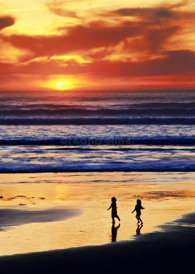 Joyful children run on a beach at sunset with breaking waves and dramatic sky. Joyful children run on a beach at sunset with breaking waves and dramatic sky