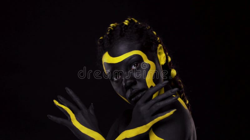 Sztuka twarzy. tańcząca kobieta z czarno-żółtą farbą do ciała. młoda afrykańska dziewczyna z kolorową farbą ciała. niesamowite afr