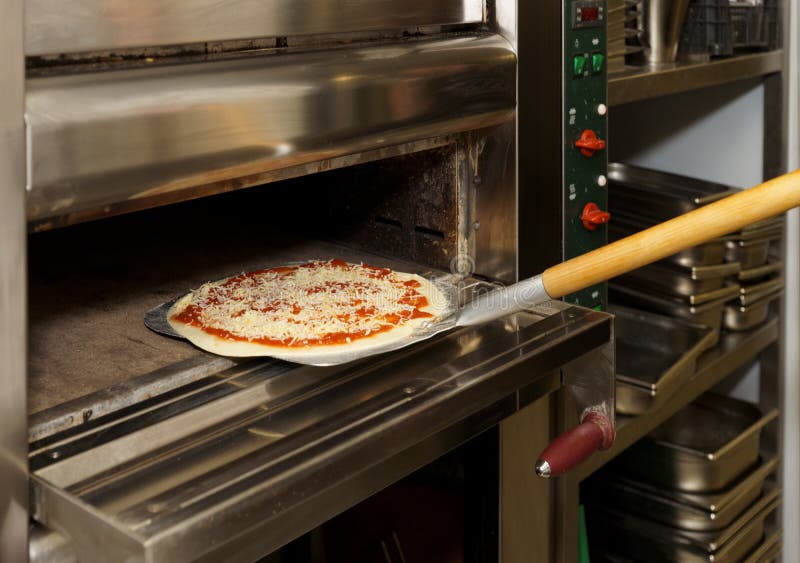 Putting pizza in oven at restaurant kitchen. Putting pizza in oven at restaurant kitchen