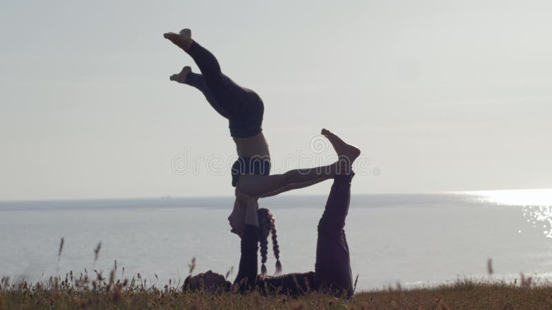 S?ance d'entra?nement au fond de nature, yoga de pratique d'acro de couples sportifs sur le pr? sur le fond de la mer et coucher