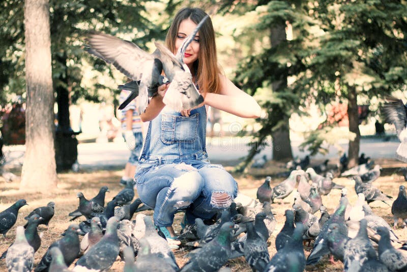 Séance de femme et graines de pigeons d'alimentations photographie stock libre de droits Séance de femme et graines de pigeons d'alimentations photographie stock libre de droits