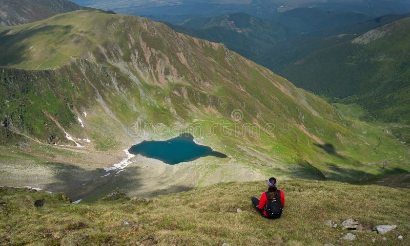 Séance de jeune femme et admirer un beau lac dans les montagnes photographie stock libre de droits Séance de jeune femme et admirer un beau lac dans les montagnes photographie stock libre de droits