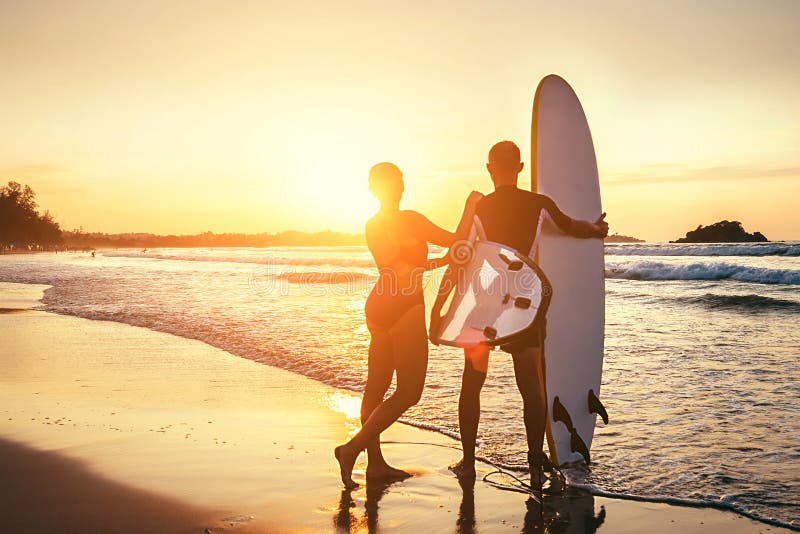 Séjour de surfers de couples sur la plage d'océan de coucher du soleil photos libres de droits Séjour de surfers de couples sur la plage d'océan de coucher du soleil photos libres de droits