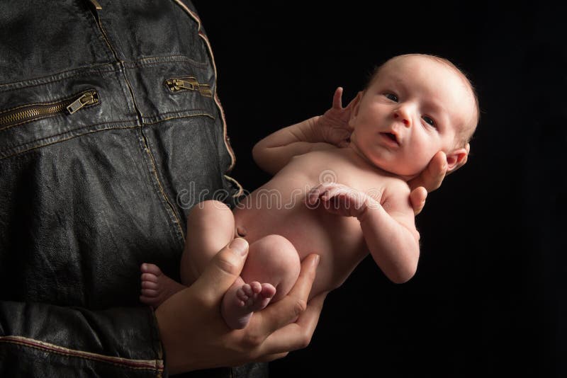 A father in a motorcyclist jacket holds his newborn son. A father in a motorcyclist jacket holds his newborn son