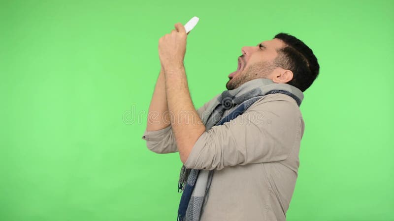 Síntomas de la gripe Joven enfermo en camisa y gran bufanda caliente estornudando duro en servilleta fondo verde, clave croma almacen de metraje de vídeo