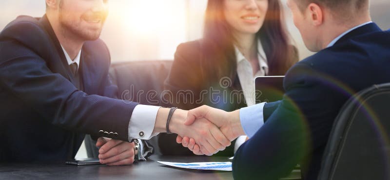 Sócios financeiros do aperto de mão que sentam-se na tabela fotografia de stock royalty free Sócios financeiros do aperto de mão que sentam-se na tabela fotografia de stock royalty free