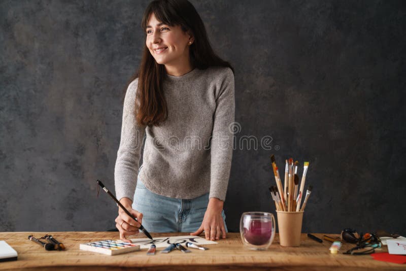 Sömmande kalligrapher-flicka som skriver med pensel när hon arbetar vid bord arkivbild