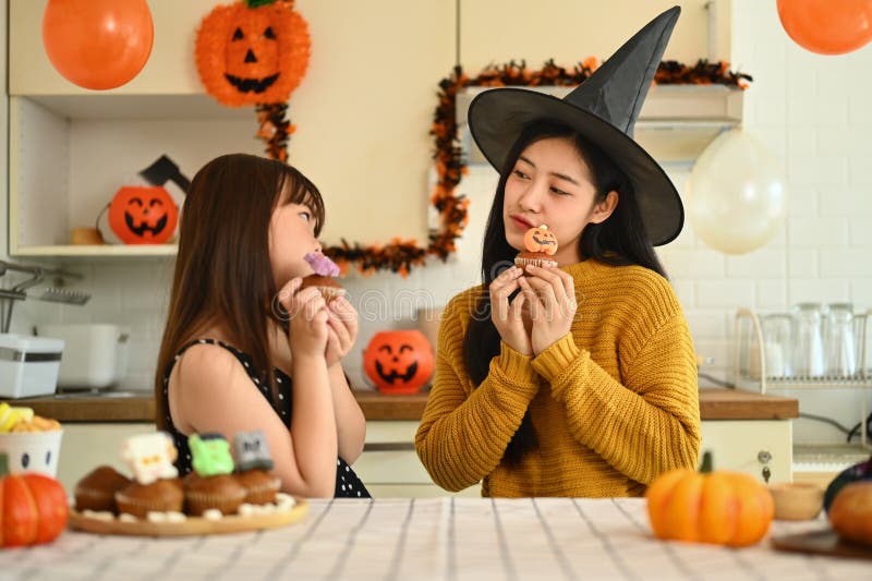 Sömmande ung mor och hennes lilla dotter som gör halloween cupcakes i köket redo för semestern royaltyfria foton