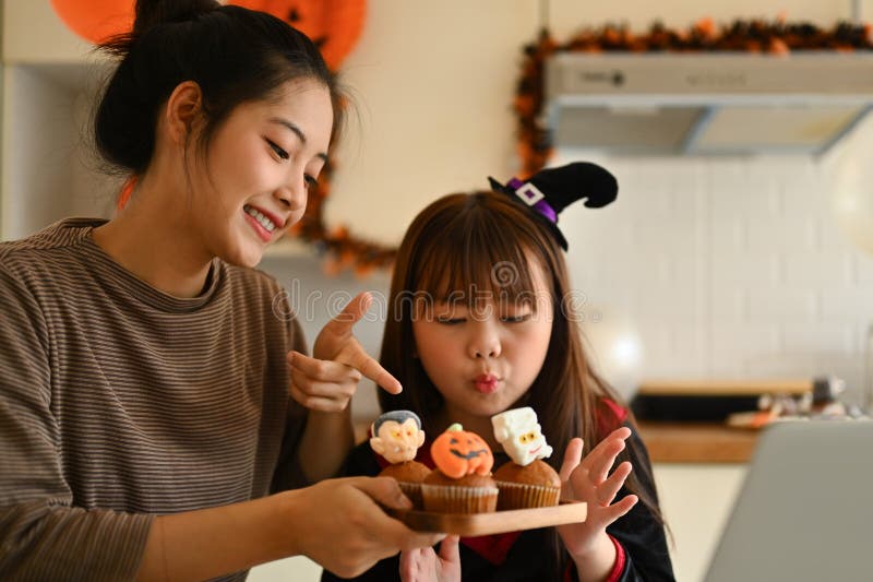 Sömmande ung mor och liten flicka med videosamtal som visar halloween cupcakes framför den bärbara datorn arkivfoto
