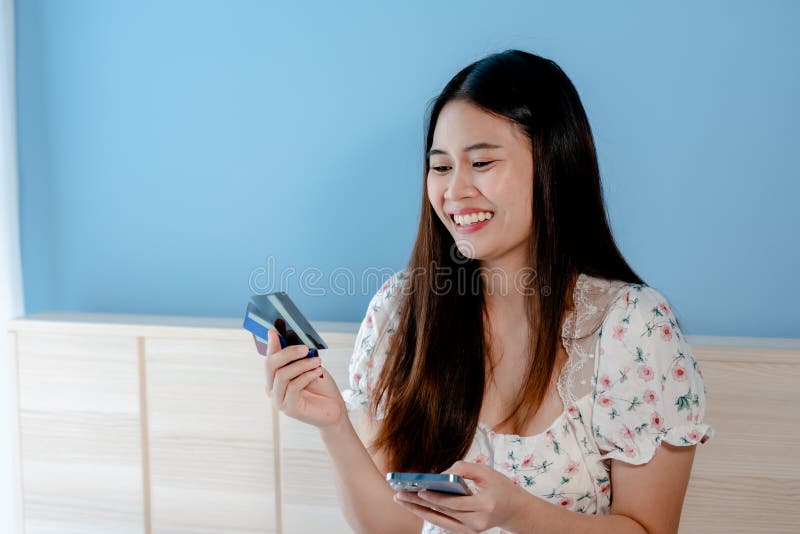 Cute Asian woman looking at 3 credit cards to choose to use for online shopping with the laptop in front of her bedroom.with a happy smiling face. Cute Asian woman looking at 3 credit cards to choose to use for online shopping with the laptop in front of her bedroom.with a happy smiling face