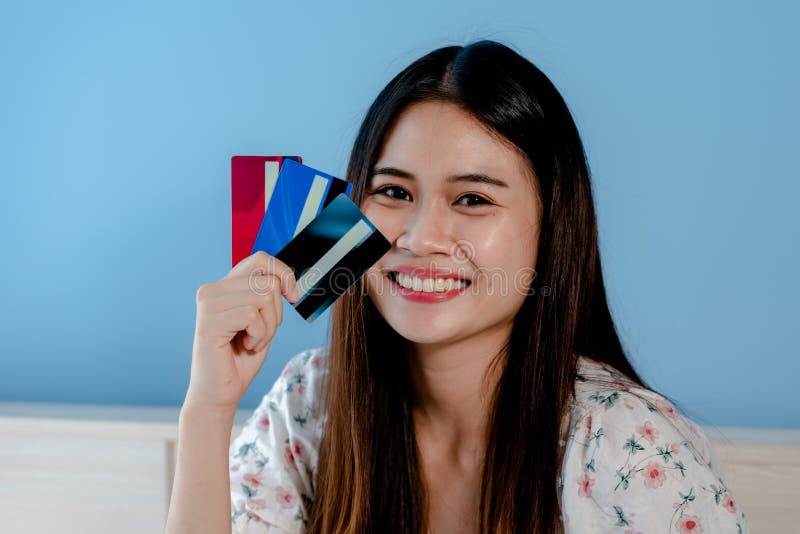 Cute Asian woman looking at 3 credit cards to choose to use for online shopping with the laptop in front of her bedroom.with a happy smiling face. Cute Asian woman looking at 3 credit cards to choose to use for online shopping with the laptop in front of her bedroom.with a happy smiling face.