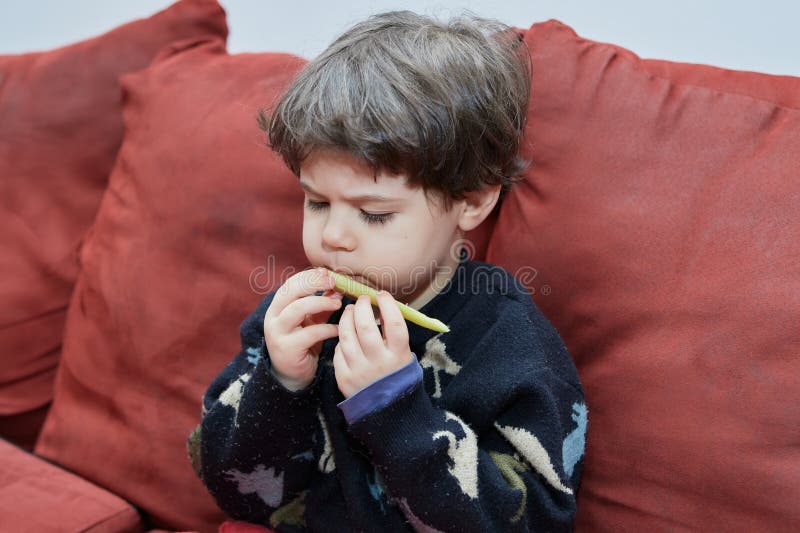 Söt babypojke som äter en gurka på soffan i sin dinasaur-pyjamas royaltyfri fotografi