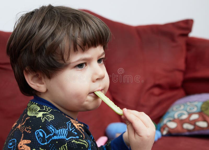 Söt babypojke som äter en gurka på soffan i sin dinasaur-pyjamas royaltyfri bild