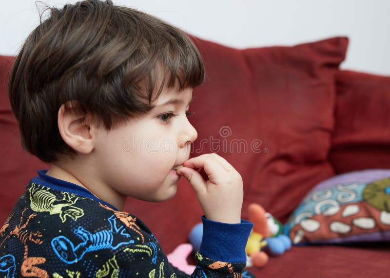 Söt babypojke som äter en gurka på soffan i sin dinosauripyjamas arkivbild