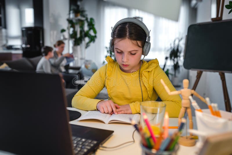 Söt barn med hörlurar som använder en bärbar dator för onlineutbildning. hemskola. tjej som gör hemläxor hemma royaltyfri bild