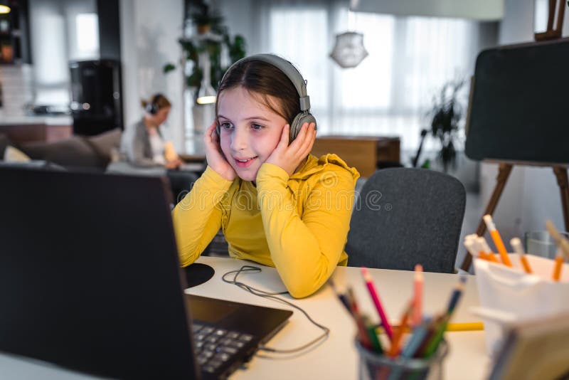 Söt barn med hörlurar som använder en bärbar dator för onlineutbildning. hemskola. tjej som gör hemläxor hemma royaltyfria foton