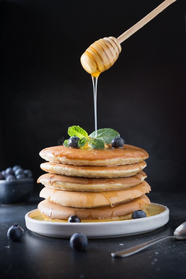 Söt hemlagad bunt av pannkakor med det nya blåbäret, honung och mintkaramellen i modern platta på svart arkivfoton Söt hemlagad bunt av pannkakor med det nya blåbäret, honung och mintkaramellen i modern platta på svart arkivfoton