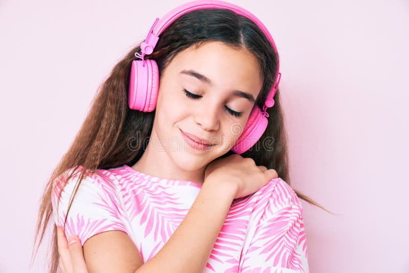 Söt, hisnande, barnflicka som lyssnar på musik med hörlurar som kramar sig själv glad och positiv och leende självsäker fotografering för bildbyråer