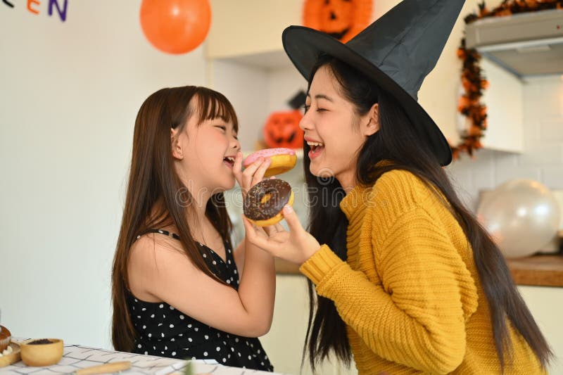 Söt liten flicka och mor som äter söt donut i köket. halloween-festbegrepp arkivfoto