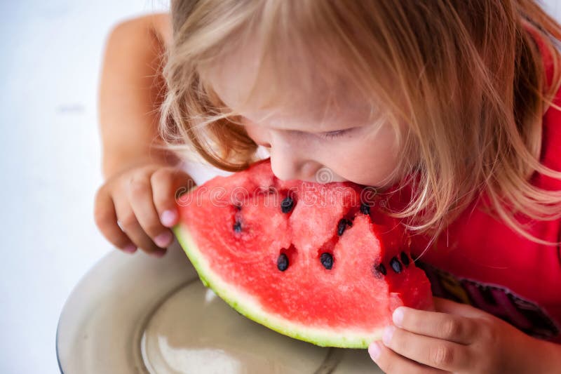Söt liten flicka 4 år åt vattenmelonklossar hemma. Lustigt, blond, underordnad porträtt med vattenmelon inomhus uppåt royaltyfri foto