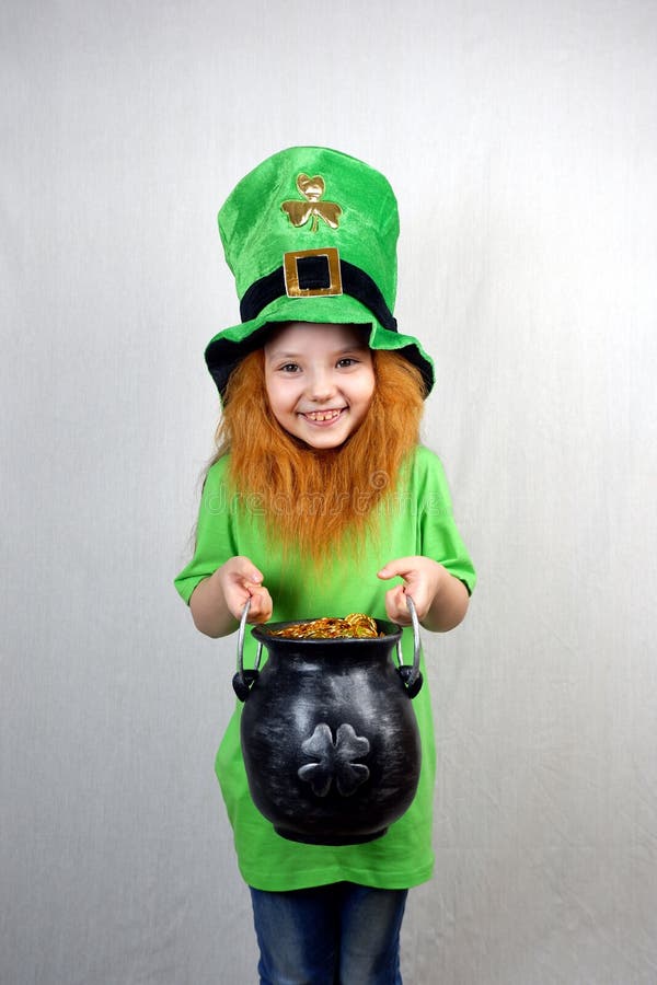 Söt skrattande liten flicka med dekorativt rött skägg i grön klänning och leprechaunhatt med gjutjärnsburk royaltyfria foton