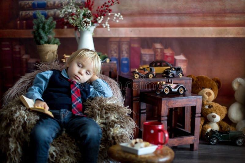 Söt småbarn somnar på liten babysoffa när man läser bok hemma arkivbild