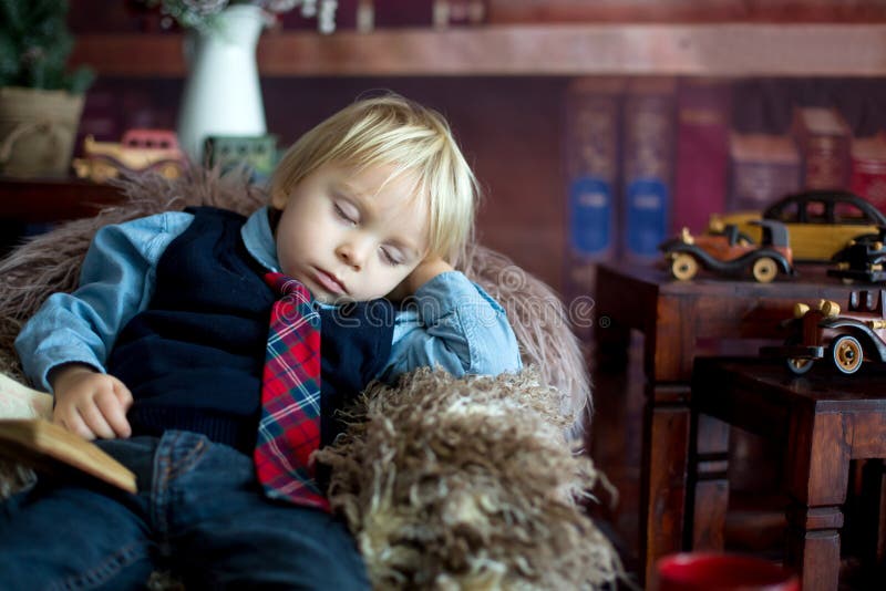 Söt småbarn somnar på liten babysoffa när man läser bok hemma arkivfoto