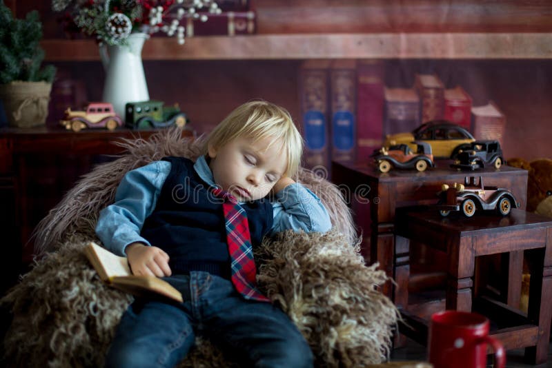 Söt småbarn somnar på liten babysoffa när man läser bok hemma royaltyfri bild