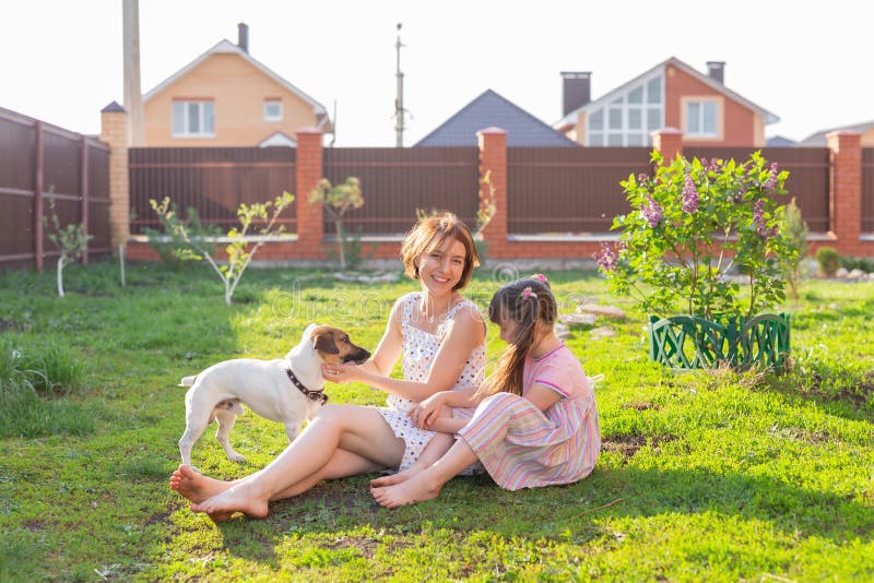 Söt ung mor och dotter sitter på gräset i sitt hemhus barefoot bredvid sin älskade hund på en solig nyck royaltyfria foton