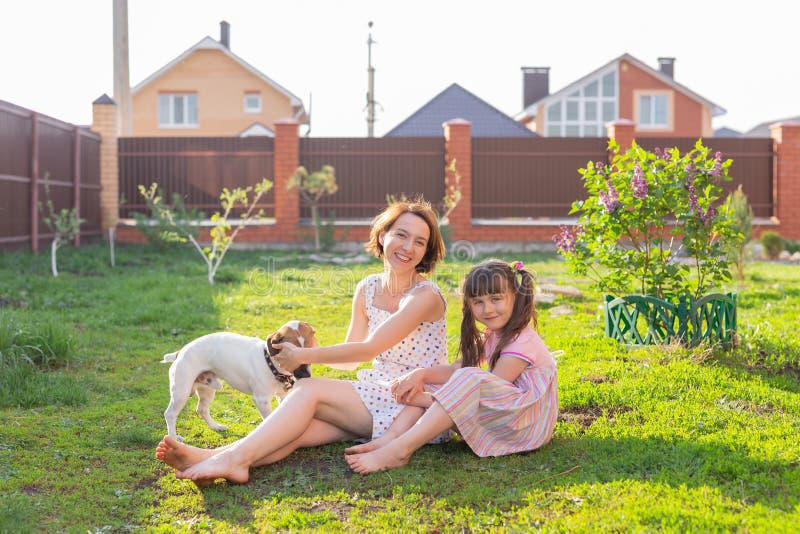 Söt ung mor och dotter sitter på gräset i sitt hemhus barefoot bredvid sin älskade hund på en solig nyck royaltyfri fotografi