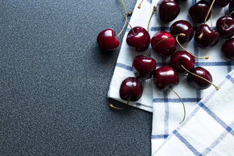 Söta mörka körsbär och kökshandduk med en linje Top besk?dar royaltyfri fotografi Söta mörka körsbär och kökshandduk med en linje Top besk?dar royaltyfri fotografi