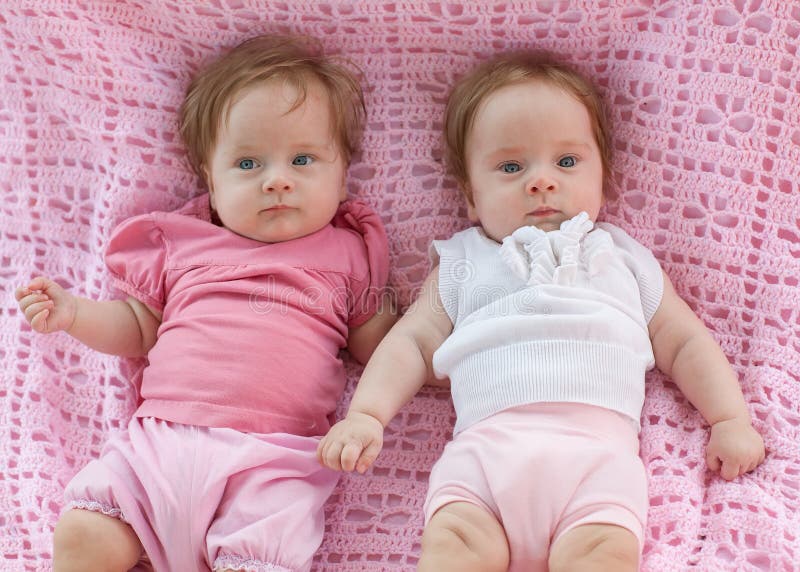 Süße kleine Zwillinge, die auf einer rosa Decke liegen. lizenzfreie stockbilder Süße kleine Zwillinge, die auf einer rosa Decke liegen. lizenzfreie stockbilder
