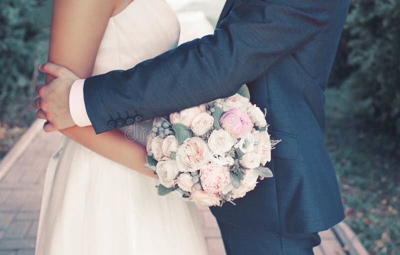 Süßes Hochzeitspaar mit leichtem Blumenstrauß von Pfingstrosen blüht, der sinnliche Bräutigam, der reizende Braut umarmt lizenzfreies stockfoto Süßes Hochzeitspaar mit leichtem Blumenstrauß von Pfingstrosen blüht, der sinnliche Bräutigam, der reizende Braut umarmt lizenzfreies stockfoto