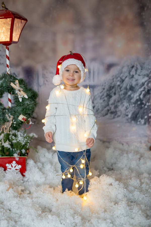 Cute toddler boy, blond child, standing in front of the house, wrapped in christmas string lights, feeling trapped. Cute toddler boy, blond child, standing in front of the house, wrapped in christmas string lights, feeling trapped