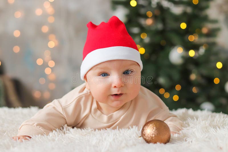Süßes Kleinkind in roten Weihnachten, der auf seinem Bauch liegt. Baby in einer neuen Kostümverengung vor dem Hintergrund lizenzfreies stockfoto