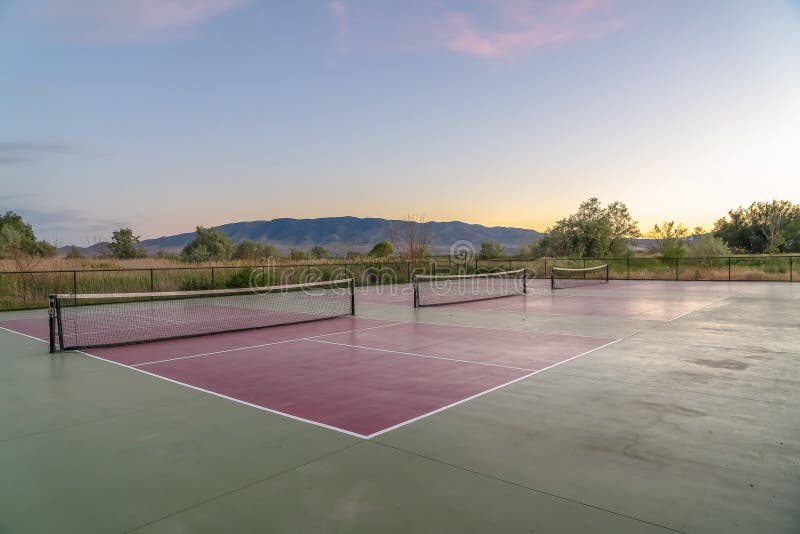 Tennis courts with an amazing view of mountain blue sky and glowing sunset. An expansive grassy terrain can also be seen around the sports area. Tennis courts with an amazing view of mountain blue sky and glowing sunset. An expansive grassy terrain can also be seen around the sports area.