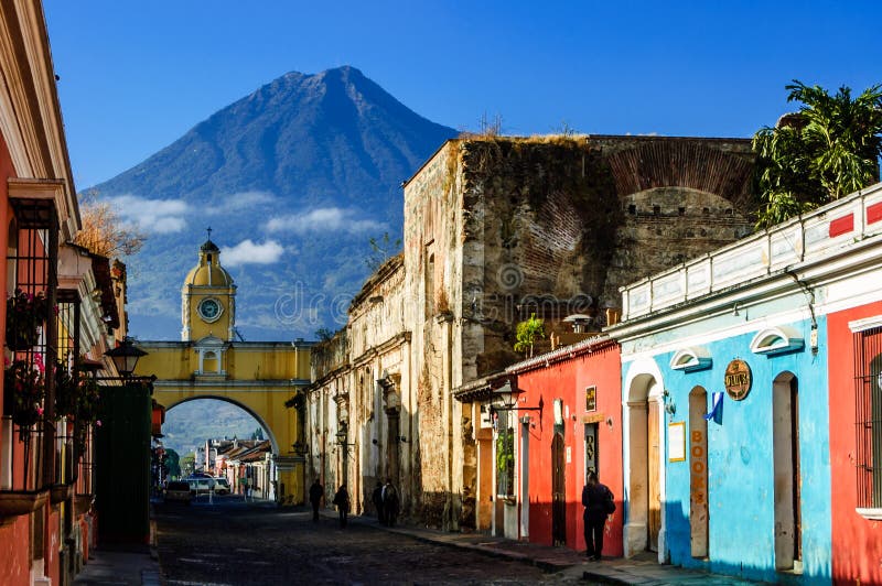 Antigua, Guatemala - March 11 2012: Locals walk to work along cobbled street with Agua volcano behind Santa Catalina Arch in Spanish colonial town & UNESCO World Heritage Site. Antigua, Guatemala - March 11 2012: Locals walk to work along cobbled street with Agua volcano behind Santa Catalina Arch in Spanish colonial town & UNESCO World Heritage Site.