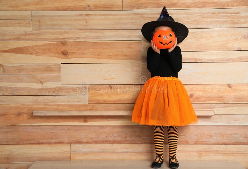 Słodka mała dziewczynka z dyniowatym wiadrem w kostiumie Halloween w pobliżu drewnianej ściany obrazy royalty free