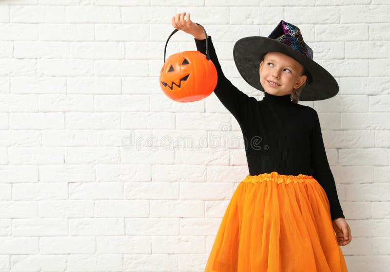 Słodka mała dziewczynka z dynią w kubełku z kostiumem Halloween w pobliżu białej ceglanej ściany zdjęcie royalty free