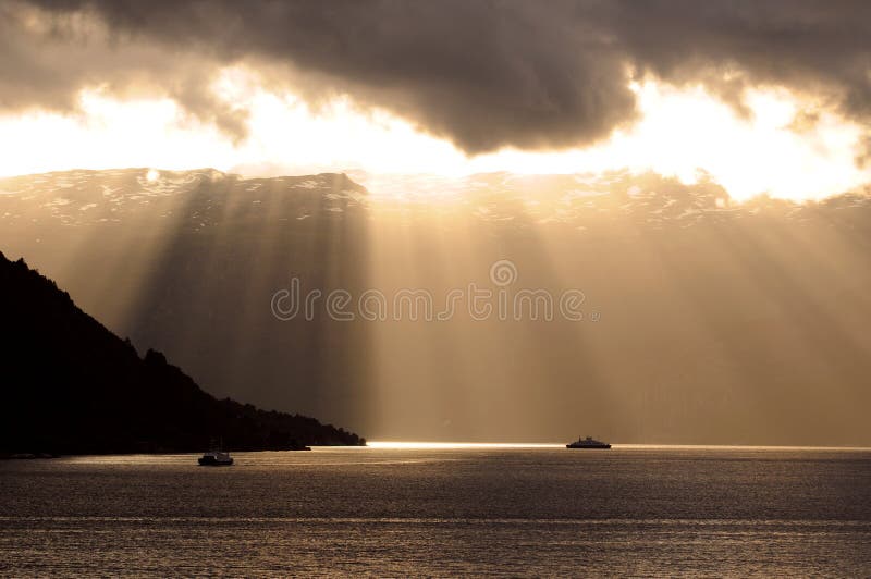 Golden sun rays through clouds falling on calm seawater. Golden sun rays through clouds falling on calm seawater.