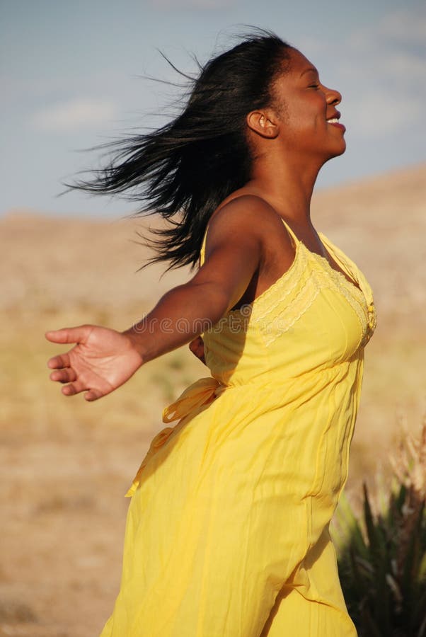 Profile shot of a beautiful African American woman wearing a yellow summer dress in the desert. She is holding both arms out behind her and enjoying the breeze. Profile shot of a beautiful African American woman wearing a yellow summer dress in the desert. She is holding both arms out behind her and enjoying the breeze.